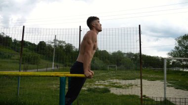 Genç sporcu doğada paralel barlarda şınav çekiyor. Spor alanında egzersiz yapan güçlü bir sporcu. Erkek üstsüz sporcu dışarıda sıkı çalışıyor. Aktif spor yaşam tarzı kavramı. Yavaş çekim