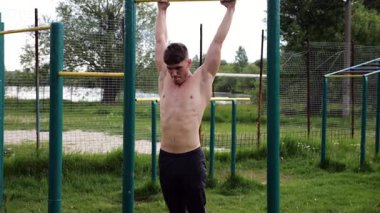 Atletik adam karın kaslarını eğitir spor sahasında yatay barda bacak kaldırır. Genç sporcu, barfiks çekme çubuğunda egzersiz yapıyor. Doğada spor yapan sporcu. Sağlıklı yaşam tarzı.