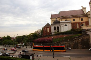 Bahar caddesinde çiçek açan ağaçlar ve şehir trafiğiyle tarihi kilisenin önünden geçen modern tramvay.