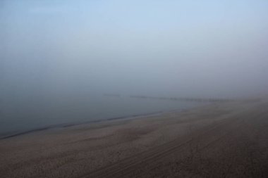 Issız kumlu sahil ve sakin deniz Yoğun sabah sisi Ufukta çok az görünen ahşap dalgalar