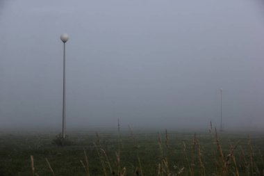 Gerçeküstü ve kasvetli bir sabah sislerin içinde kaybolan sokak lambalarıyla minimalist sisli bir tarla.