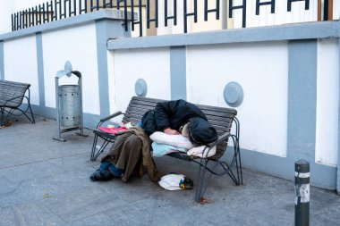 unrecognizable homeless man sleeping on bench near church fence.