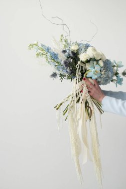 A hand gracefully holds a stunning bouquet filled with delicate blue and white flowers, accentuated by greenery and ribbons, illuminated by soft light. clipart