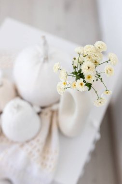 Beyaz balkabakları ve narin çiçeklerle süslenmiş bir vazo içeren sakin bir düzenleme sonbahar dekorasyonu için mükemmel sıcak ve davetkar bir atmosfer yaratır..