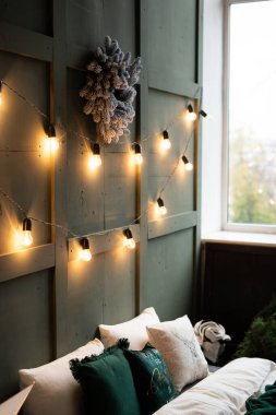 Sakin bir kış öğleden sonrasında, sıcak sicim ışıkları ve dekoratif çelenkle süslenmiş rahat bir yatak odası.