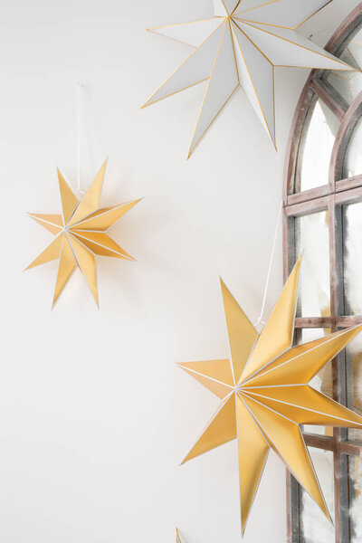 Золотые и серебряные декоративные звезды висят у окна в уютном интерьере, создавая теплую атмосферу в праздничный сезон