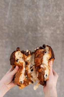 A person holding a freshly baked chocolate chip bread loaf with gooey interior in front of a gray backdrop clipart