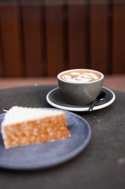 Öğleden sonra dinlenme sırasında bir dilim kek ve latte sanatıyla rahat kahve seti.