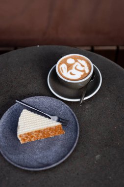Kahve ve latte sanatıyla nefis bir kahve ve öğleden sonra sıcak bir kafede siyah bir masada bir dilim kek.