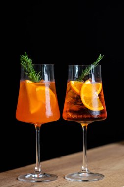 Two refreshing cocktails with orange slices and rosemary garnishes served in elegant glasses against a dark background clipart