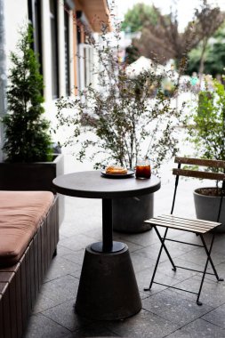 Cozy outdoor caf setup with a small round table, a pastry, and a drink on a sunny day in an urban setting clipart