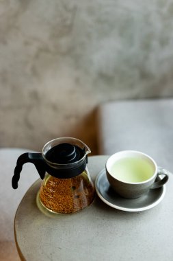 Öğleden sonra sıcacık bir kafede minimalist bir masada çaydanlığın yanında dumanı tüten yeşil bir çay.