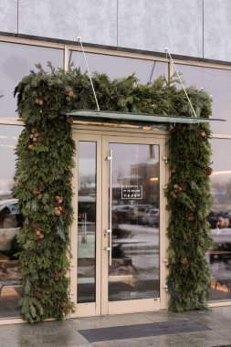 A beautifully adorned entrance with greenery and pine cones welcoming visitors during the winter season at a modern building clipart