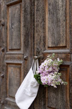 A rustic wooden door adorned with a bouquet of delicate flowers and a simple tote bag in a charming village setting clipart