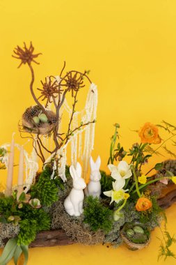 Tavşanlarla, canlı çiçeklerle ve güneşli sarı bir zeminde doğal elementlerle tuhaf bir bahar düzenlemesi.