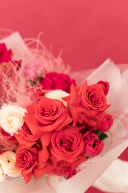 Canlı bir buket kırmızı ve pembe gül yumuşak pembe bir zemine karşı dizilmiş, kutlama ve romantik jestler için mükemmel.