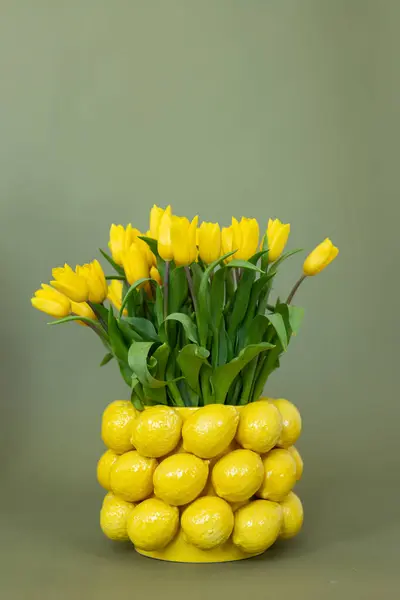 Limon temalı yaratıcı bir vazoda sergilenen neşeli sarı laleler bir bahar gününün tazeliğini artırıyor.