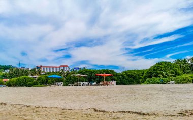 Palmiye ağaçları, şemsiyeler ve güneş şemsiyeleri Zicatela Puerto Escondido Oaxaca Meksika 'daki tropik Meksika plajındaki sahil tatil beldesi otelinde..