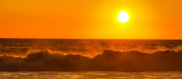 Beautiful stunning colorful and golden sunset in yellow orange red on beach and big wave panorama in tropical nature in Zicatela Puerto Escondido Oaxaca Mexico.