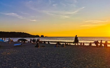 İnsanlar, Zicatela Puerto Escondido Oaxaca Mexico 'daki tropikal doğada sarı turuncu ve altın rengi günbatımını izliyorlar..