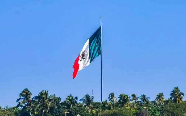Mexican green white red flag with palm trees and blue sky and clouds in Zicatela Puerto Escondido Oaxaca Mexico.