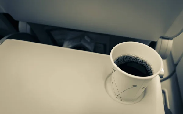 Coffee mug with black coffee in the plane on a folding table. Eating and drinking on the plane.