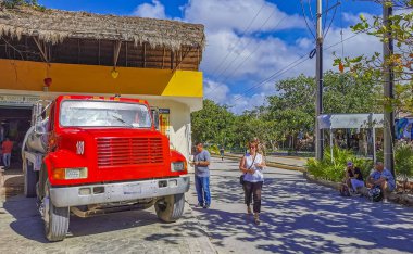 Tulum Mexico 09. March 2022 Typical colorful street road red water truck and cityscape with cars traffic palm tourism shops bars and restaurants of Tulum in Mexico.