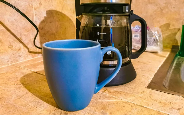 Blue coffee cups and black coffee maker from Mexico on cream background in clean kitchen.