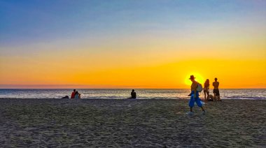 People are watching beautiful stunning colorful and golden sunset in yellow orange red on beach and big huge surfer wave panorama in tropical nature in Zicatela Puerto Escondido Oaxaca Mexico.