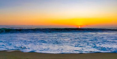 Beautiful stunning colorful and golden sunset in yellow orange red on beach and big huge surfer wave panorama in tropical nature in Zicatela Puerto Escondido Oaxaca Mexico.