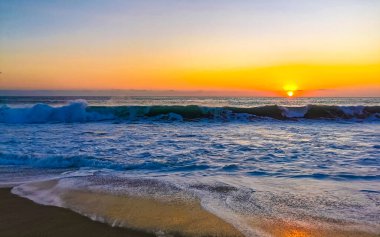 Beautiful stunning colorful and golden sunset in yellow orange red on beach and big huge surfer wave panorama in tropical nature in Zicatela Puerto Escondido Oaxaca Mexico.