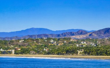 Zicatela Puerto Escondido Oaxaca 'da güneş kumsalı uçurumları dağlar, palmiye ağaçları, mavi sular ve gökyüzü dalgalanır..