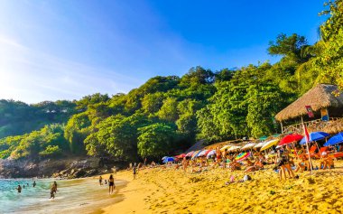 Puerto Escondido Oaxaca Meksika 14. Kasım 2022 Sahil Kum Turkuvaz Mavi Su Kayalıkları Kayalar Güneş Kayaları Palmiye ağaçları ve Playa Carrizalillo sahilinde büyük sörfçü dalgaları Puerto Escondido Oaxaca Meksika.