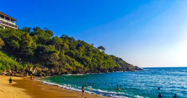 Puerto Escondido Oaxaca Mexico 14. November 2022 Beach sand turquoise blue water rocks cliffs boulders sun loungers people palm trees and huge big surfer waves on the beach Playa Carrizalillo in Puerto Escondido Oaxaca Mexico. clipart