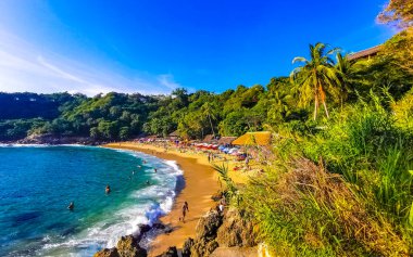 Puerto Escondido Oaxaca Meksika 14. Kasım 2022 Sahil Kum Turkuvaz Mavi Su Kayalıkları Kayalar Güneş Kayaları Palmiye ağaçları ve Playa Carrizalillo sahilinde büyük sörfçü dalgaları Puerto Escondido Oaxaca Meksika.