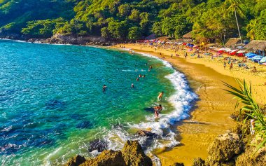 Puerto Escondido Oaxaca Meksika 14. Kasım 2022 Sahil Kum Turkuvaz Mavi Su Kayalıkları Kayalar Güneş Kayaları Palmiye ağaçları ve Playa Carrizalillo sahilinde büyük sörfçü dalgaları Puerto Escondido Oaxaca Meksika.