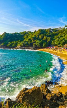 Puerto Escondido Oaxaca Meksika 14. Kasım 2022 Sahil Kum Turkuvaz Mavi Su Kayalıkları Kayalar Güneş Kayaları Palmiye ağaçları ve Playa Carrizalillo sahilinde büyük sörfçü dalgaları Puerto Escondido Oaxaca Meksika.