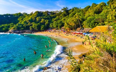 Puerto Escondido Oaxaca Meksika 14. Kasım 2022 Sahil Kum Turkuvaz Mavi Su Kayalıkları Kayalar Güneş Kayaları Palmiye ağaçları ve Playa Carrizalillo sahilinde büyük sörfçü dalgaları Puerto Escondido Oaxaca Meksika.