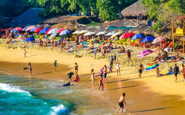 Puerto Escondido Oaxaca Meksika 14. Kasım 2022 Sahil Kum Turkuvaz Mavi Su Kayalıkları Kayalar Güneş Kayaları Palmiye ağaçları ve Playa Carrizalillo sahilinde büyük sörfçü dalgaları Puerto Escondido Oaxaca Meksika.