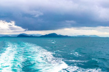 Feribotla uzun kuyruklu yat ve yüksek dalgalarla turkuvaz su plajındaki tropikal manzara manzarası boyunca Phuket adası Tayland 'daki Ratsada Amphoe Mueang Phuket' teki kireçtaşı kayaları arasında seyahat edin..