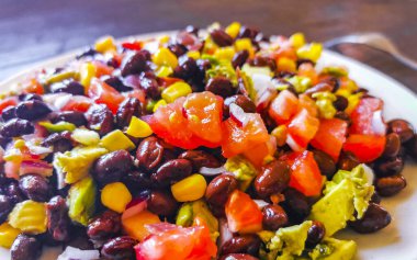 Fasulyeli sebze yemeği patates soğanlı avokado domates ve sarımsak Meksika 'da çatal veya kaşıkla beyaz bir tabak üzerinde..