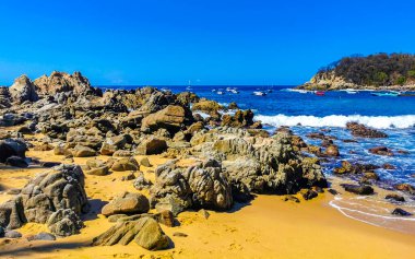 Plaj kumsalı turkuvaz mavi su kayaları kaya kayaları palmiye ağaçları büyük sörfçü dalgaları ve plaj manzarası Playa Manzanillo ve Puerto Angelito Puerto Escondido Oaxaca Meksika.