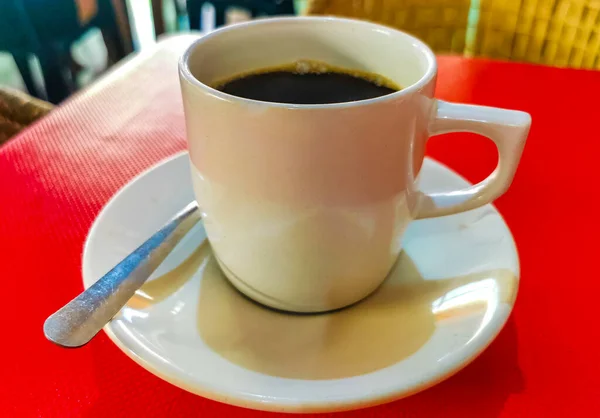 赤いテーブルの上にスプーンとプレートとアメリカーノブラックコーヒーのカップ背景の食べ物とジカテラプエルトエスコンディドオアハカメキシコのレストランで飲む — ストック写真