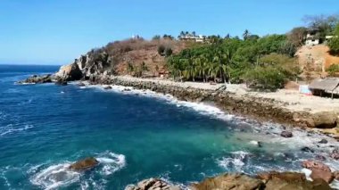 Plaj kumsalı turkuvaz mavi su kayaları kaya kayaları palmiye ağaçları büyük sörfçü dalgaları ve plaj manzarası Playa Manzanillo ve Puerto Angelito Puerto Escondido Oaxaca Meksika.