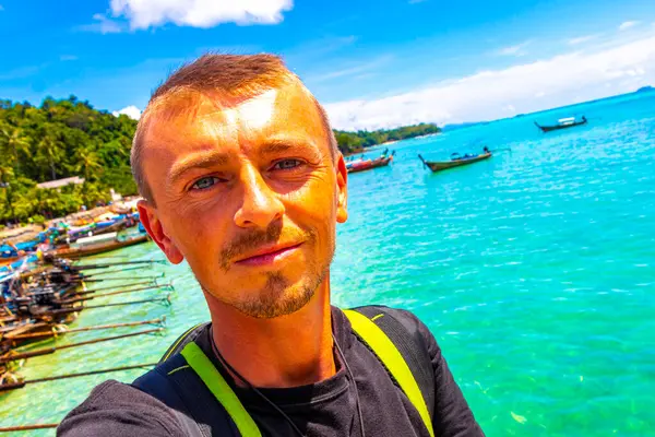 stock image Tourist traveler male person man takes selfie photo with Longtail boat boats at the beautiful famous beach lagoon between limestone rocks turquoise water Koh Phi Phi Don island Ao Nang Krabi Thailand.