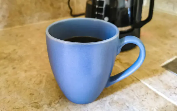 Blue coffee cups and black coffee maker from Mexico on cream background in clean kitchen.