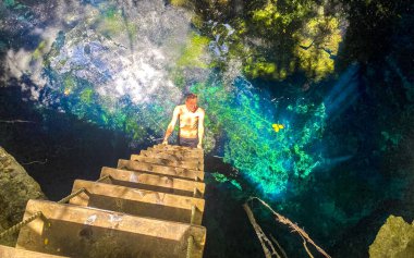 Gezgin ve turist rehberi, Puerto Aventuras Quintana Roo Mexico 'daki muhteşem mavi turkuaz suyu ve kireçtaşı mağarası çukuruna tırmanıyor..