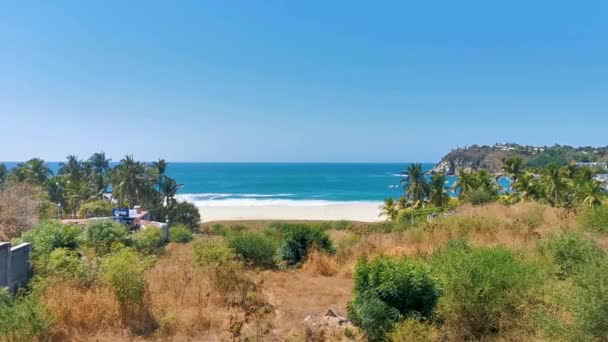 サンビーチの砂浜は ヤシの木の寄生虫が付いている水とサーファーの波は ツーリズムの崖と青空ツーリズムを岩にします プエルトエスコンディードオアハカ メキシコ — ストック動画