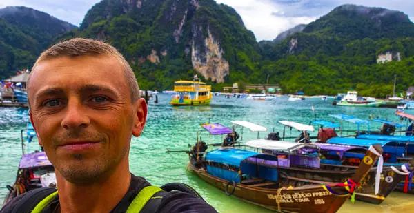 stock image Tourist traveler male person man takes selfie photo with Longtail boat boats at the beautiful famous beach lagoon between limestone rocks turquoise water Koh Phi Phi Don island Ao Nang Krabi Thailand.