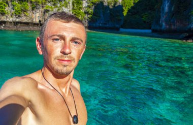 Turist erkek adam, kireçtaşından kayalar ve turkuaz mavi su Koh Phi Phi Leh adası Ao Nang Krabi Tayland arasındaki ünlü plaj gölünde selfie çekiyor..